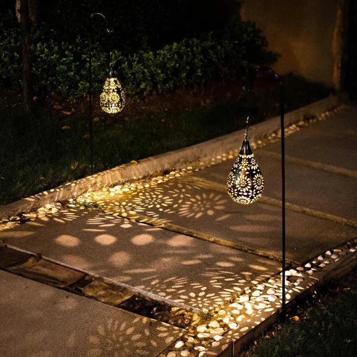 Solarbetriebene Gartenleuchte, tropfenförmig, schwarz-gold, beleuchtet Gehweg nachts.