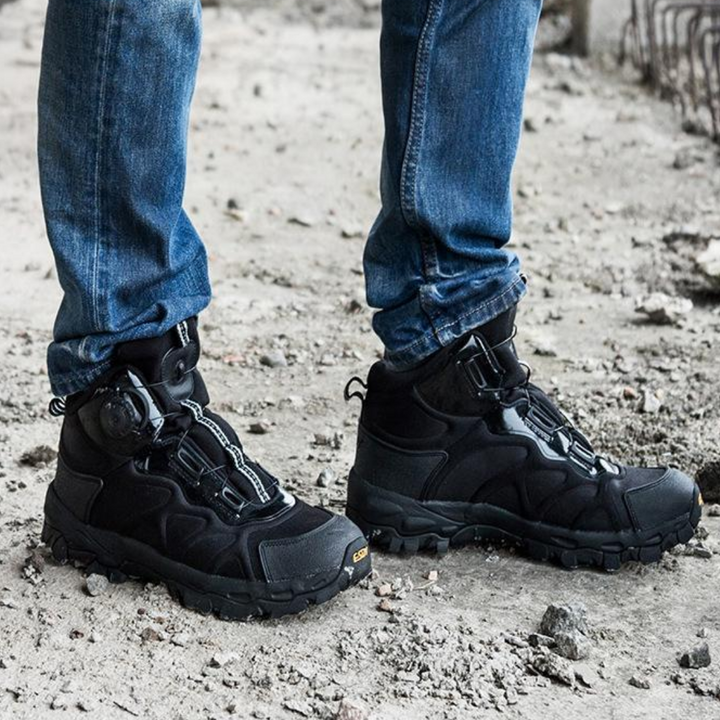 Schwarze Outdoor-Wanderschuhe, robustes Design, getragen mit blauen Jeans, auf steinigem Untergrund.