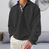 Schwarzer Herrenpullover mit Kragen, kariertes Hemd darunter, lässiger Stil, Wohnzimmer-Hintergrund.