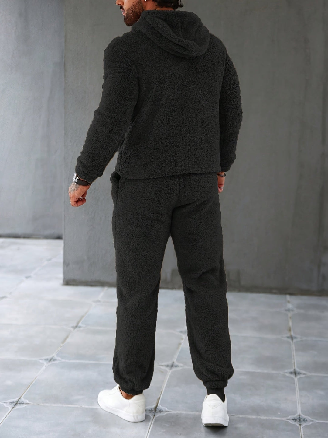 Mann in schwarzem Fleece-Trainingsanzug, Kapuze, weiße Sneaker, Rückansicht.