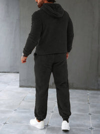 Mann in schwarzem Fleece-Trainingsanzug, Kapuze, weiße Sneaker, Rückansicht.