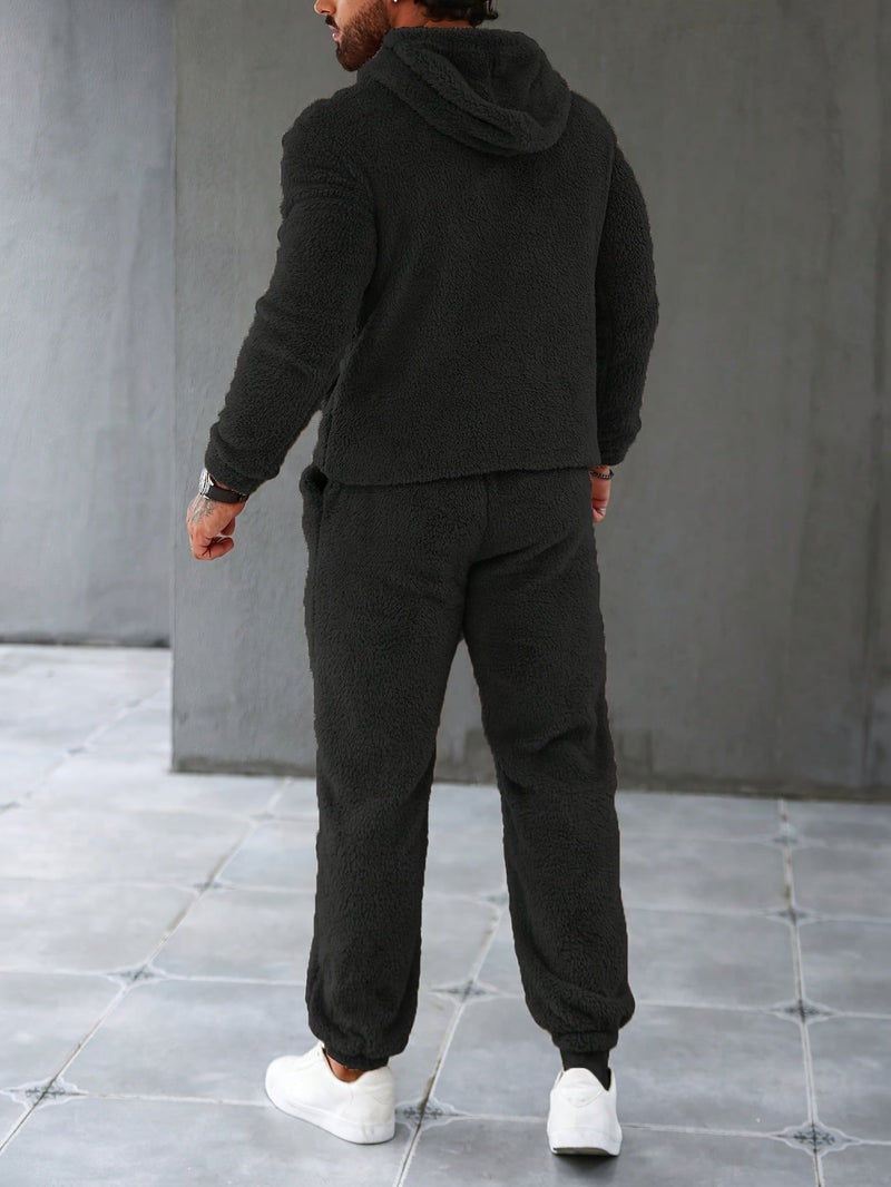 Mann in schwarzem Fleece-Trainingsanzug, Kapuze, weiße Sneaker, Rückansicht.