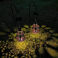 Zwei hängende Solarlaternen, tropfenförmig, mit Blumenmuster, beleuchten Rasen bei Nacht.