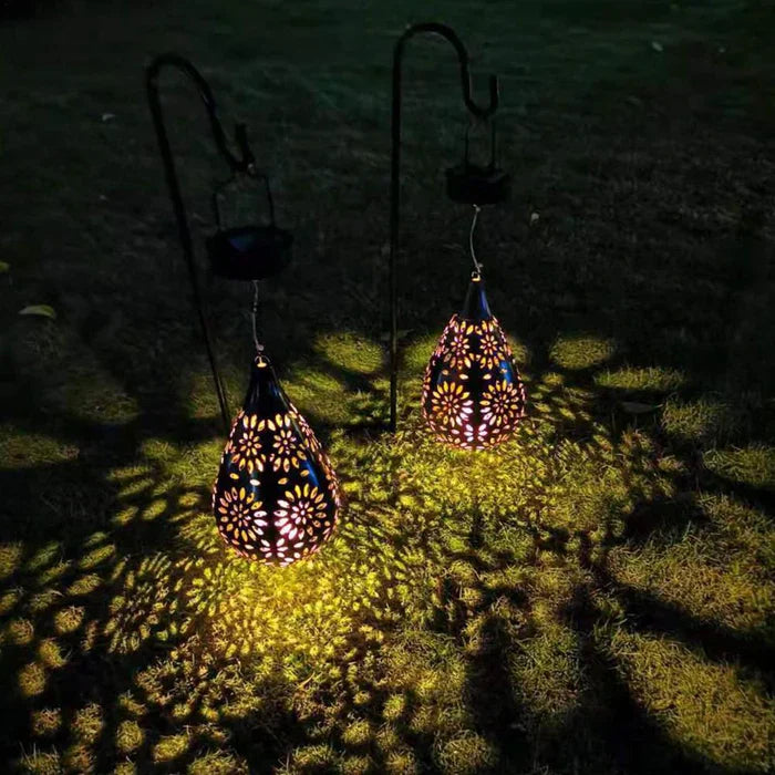 Zwei hängende Solarlaternen, tropfenförmig, mit Blumenmuster, beleuchten Rasen bei Nacht.