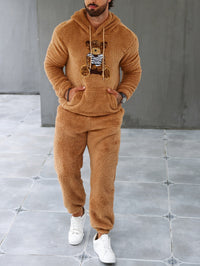 Mann in braunem Teddyfleece-Trainingsanzug mit Bärenmotiv, weiße Sneaker, modisch, gemütlich.
