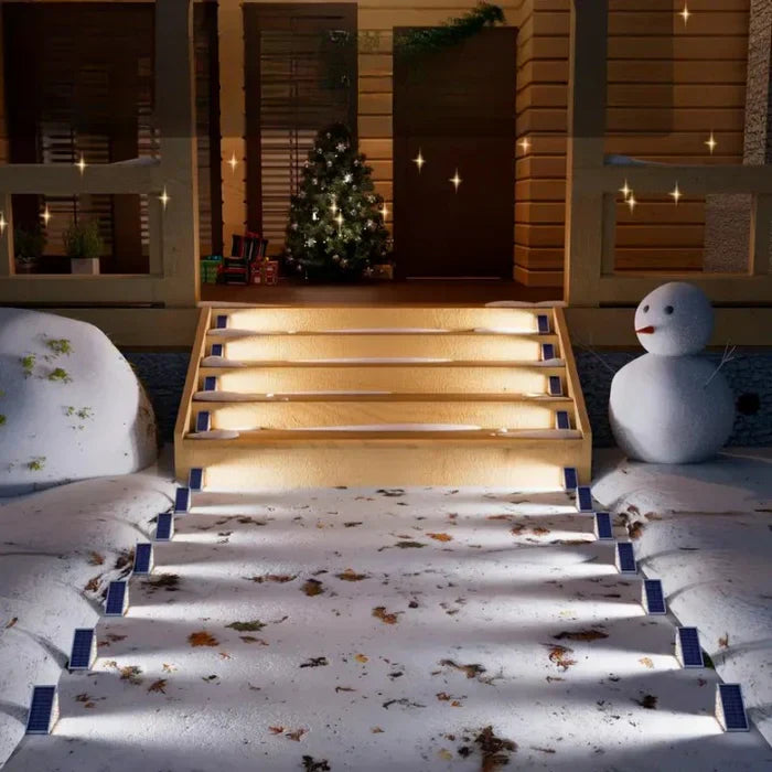 Beleuchtete Außentreppe mit Schneemann und Weihnachtsbaum, winterliche Dekoration, Nachtansicht.