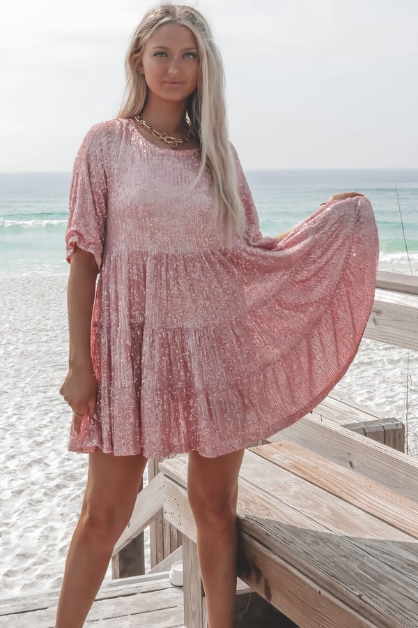 Frau in rosa Paillettenkleid am Strand, Sommermode, elegantes Freizeitoutfit, Meereshintergrund.