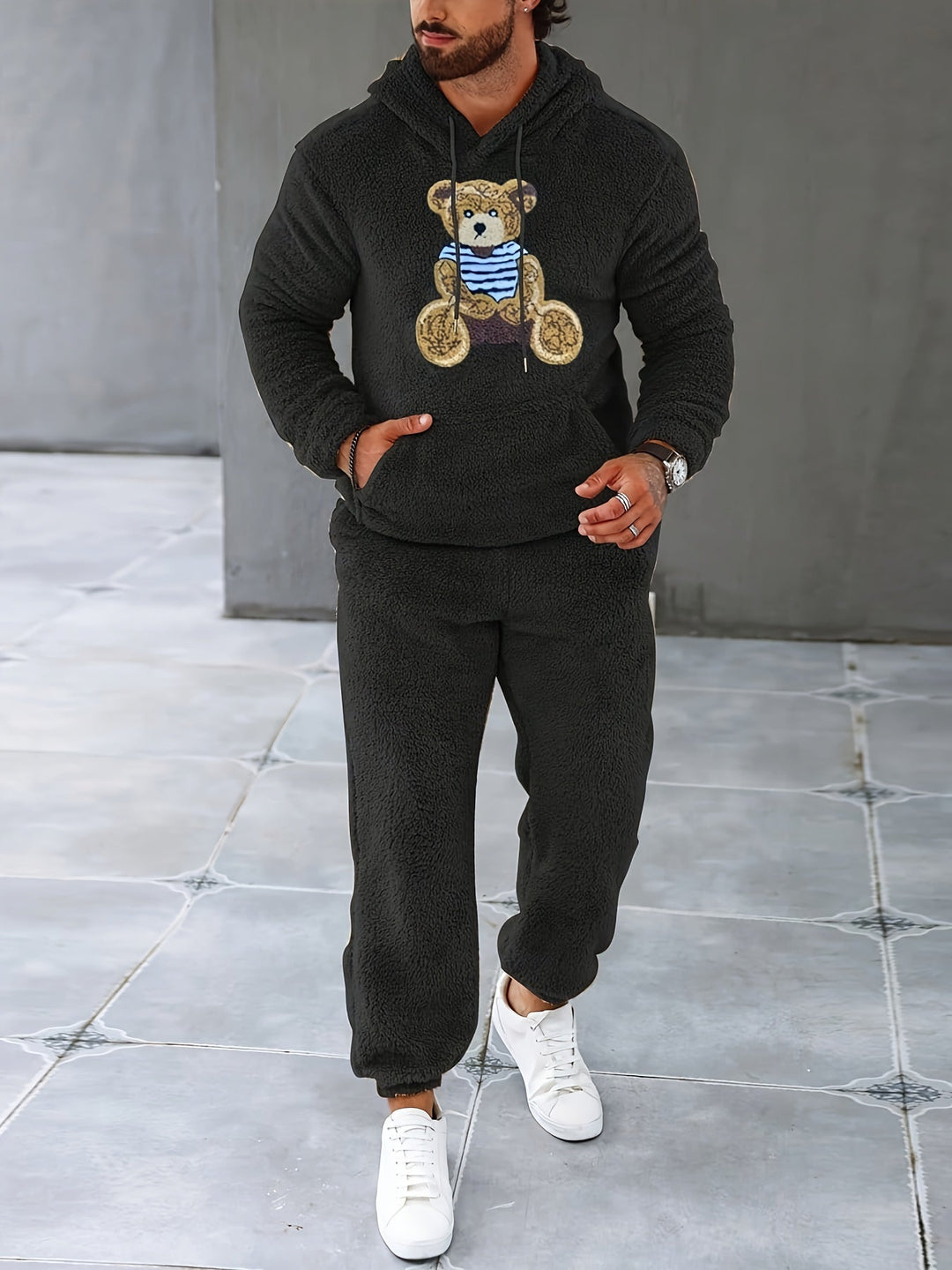 Mann in schwarzem Teddyfleece-Trainingsanzug mit Bärenmotiv, weiße Sneaker.