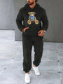 Mann in schwarzem Teddyfleece-Trainingsanzug mit Bärenmotiv, weiße Sneaker.