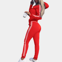 Frau in rotem Trainingsanzug mit weißen Streifen, hält Kaffeebecher, sportliche Mode.