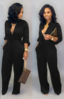 Frau in schwarzem Jumpsuit mit V-Ausschnitt, hält braune Designer-Handtasche, elegante Mode.