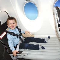 Kind sitzt im Flugzeug mit CARES-Gurt auf Flyaway Kids Bed, lächelnd, mit Stofftier.