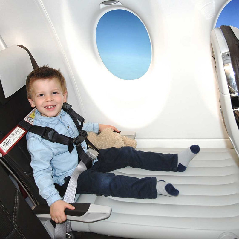 Kind sitzt im Flugzeug mit CARES-Gurt auf Flyaway Kids Bed, lächelnd, mit Stofftier.