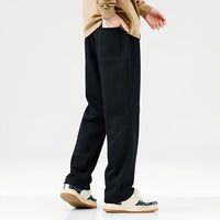 Mann in schwarzer Jogginghose und Sneakers, beige Oberteil, seitliche Ansicht.