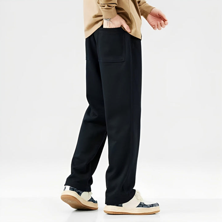 Mann in schwarzer Jogginghose und Sneakers, beige Oberteil, seitliche Ansicht.