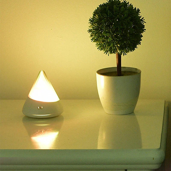 Weiße LED-Lampe in Tropfenform neben kleinem künstlichen Baum im weißen Topf auf Tisch.