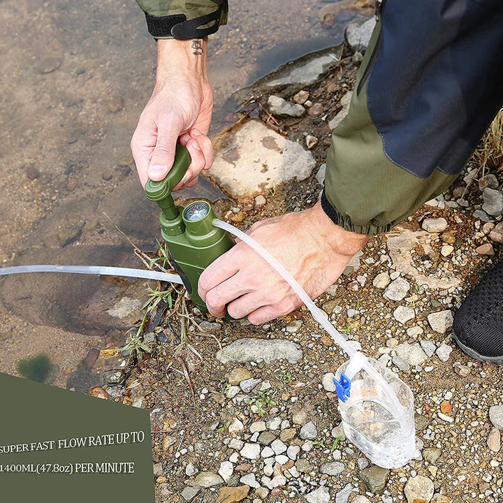 Person pumpt Wasser mit tragbarem, grünem Wasserfilter am Flussufer, Outdoor-Ausrüstung.