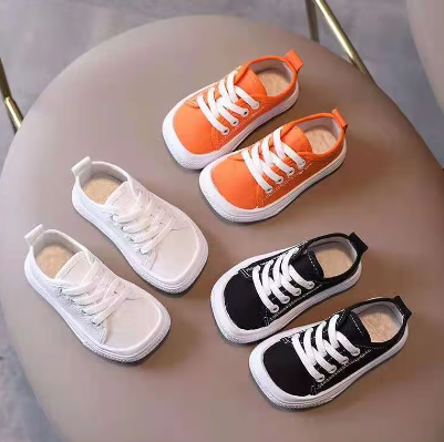 Drei Paar Kinderschuhe, weiß, orange, schwarz, auf grauem Stuhl, Sneaker, Schnürschuhe.