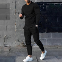 Mann in schwarzem Outfit mit weißen Sneakers vor grauer Ziegelwand, modisch, urbaner Stil.
