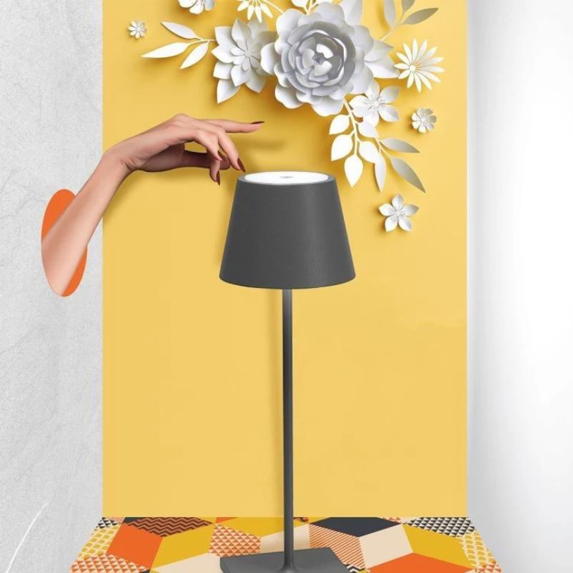 Graue Tischlampe mit schwarzem Schirm, gelber Hintergrund, dekorative Papierblumen.