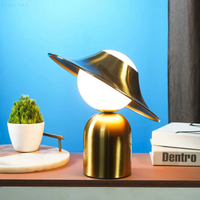 Moderne Tischlampe aus Metall, goldfarben, mit rundem Schirm, auf Holztisch vor blauem Hintergrund.
