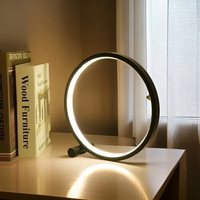Moderne LED-Tischlampe, rund, schwarz, auf weißem Tisch neben Büchern und Fenster.