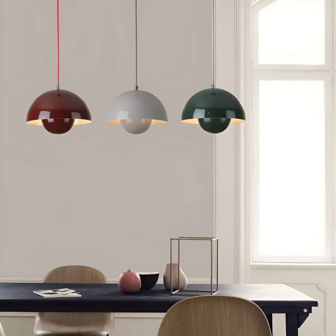 Drei moderne Pendelleuchten in Rot, Grau und Grün über einem Esstisch, skandinavisches Design.