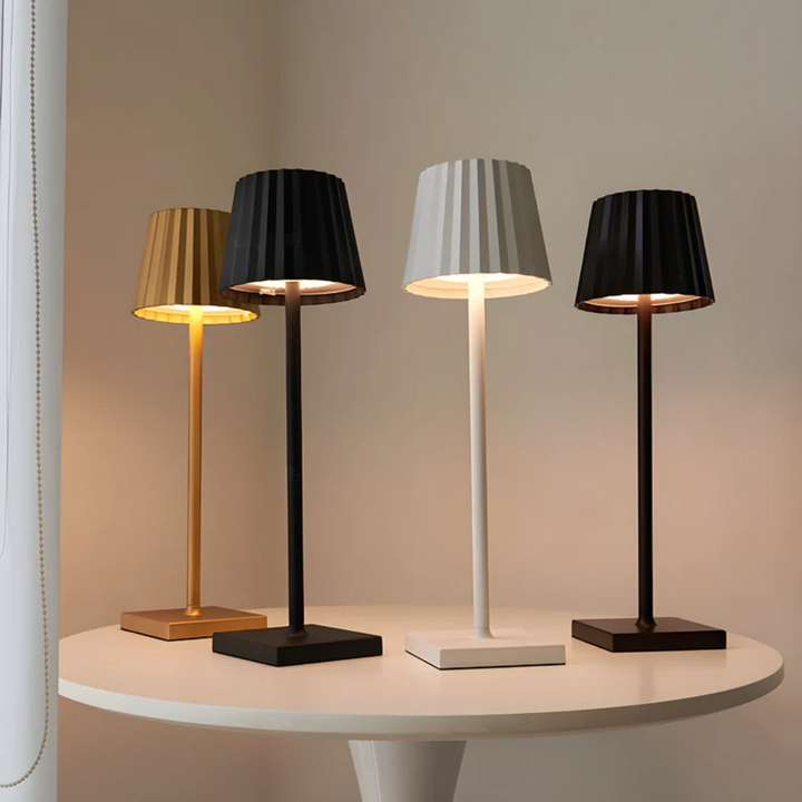 Vier moderne Tischlampen in Gold, Schwarz, Weiß und Braun auf rundem Tisch, elegantes Design.