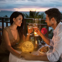 Paar beim romantischen Abendessen mit Mondlampe, Wein und Kerzenlicht auf Terrasse bei Sonnenuntergang.