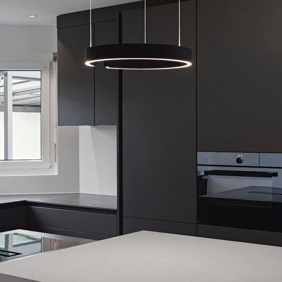 Moderne schwarze Küche mit LED-Ring-Pendelleuchte, Einbauofen und grauer Arbeitsplatte.