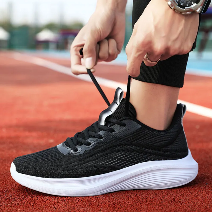 Schwarzer Sportschuh mit weißer Sohle, atmungsaktiv, ideal zum Laufen auf roter Laufbahn.
