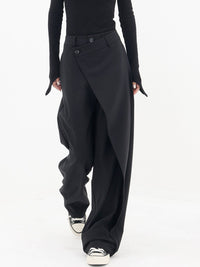 Frau trägt schwarze asymmetrische Baggy-Hose, modisch, elegant, mit Sneakers.