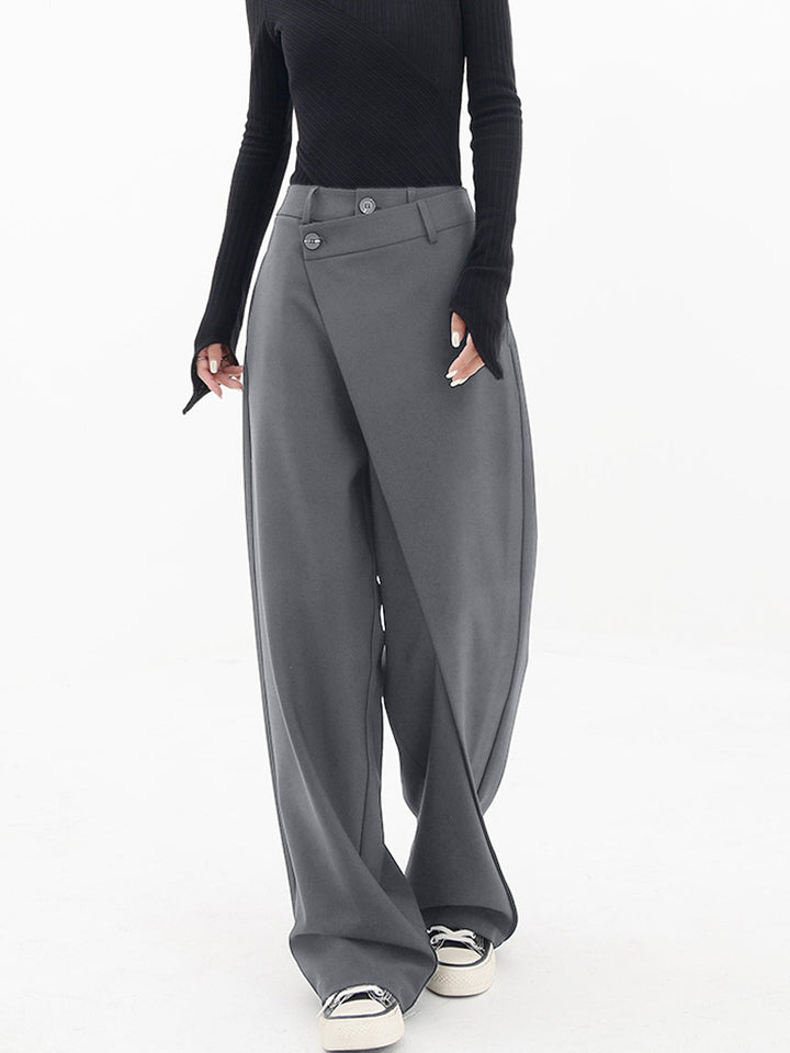 Frau trägt graue asymmetrische Baggy-Hose, modisch, elegant, mit schwarzem Oberteil.