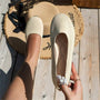 Beige Damen-Ballerinas aus Strickstoff, flach, mit Perlendetail, auf Holzterrasse.