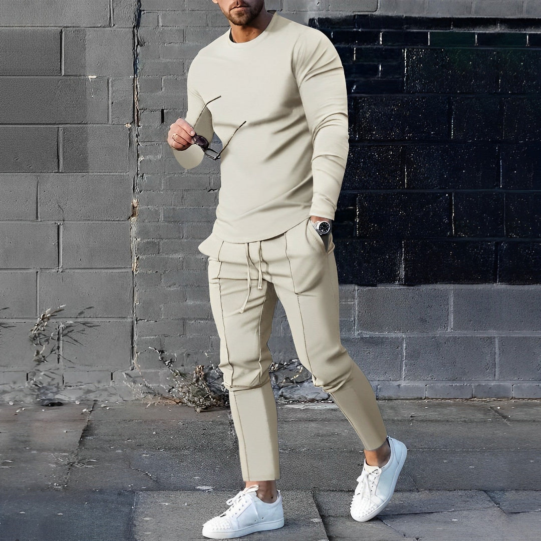 Mann in beigem Trainingsanzug, weiße Sneaker, graue Wand, urbane Mode, Freizeitkleidung.