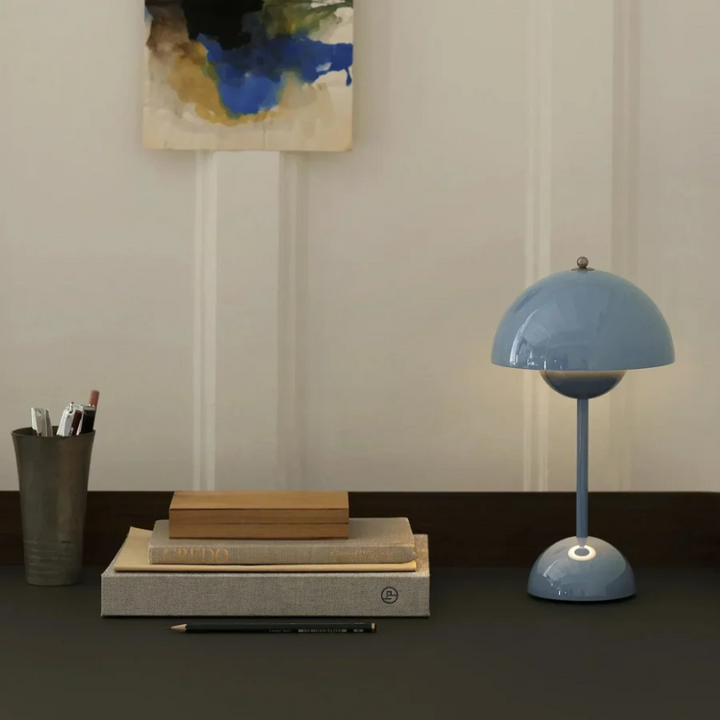 Blaue Tischlampe auf Schreibtisch mit Büchern, Stiftehalter und abstraktem Wandbild.