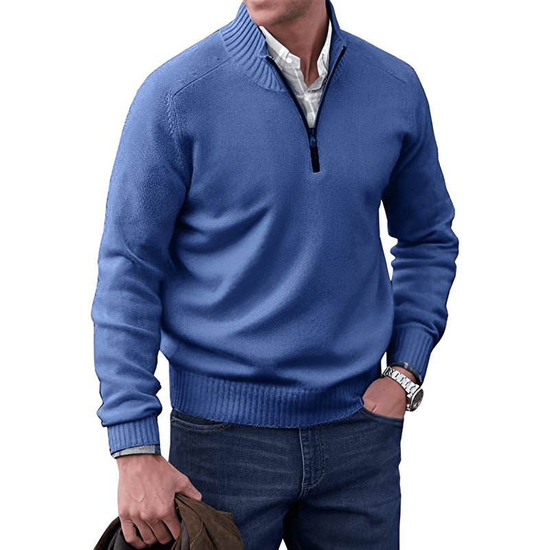 Mann in blauem Pullover mit Reißverschluss, weißem Hemd, Jeans, hält braune Jacke.
