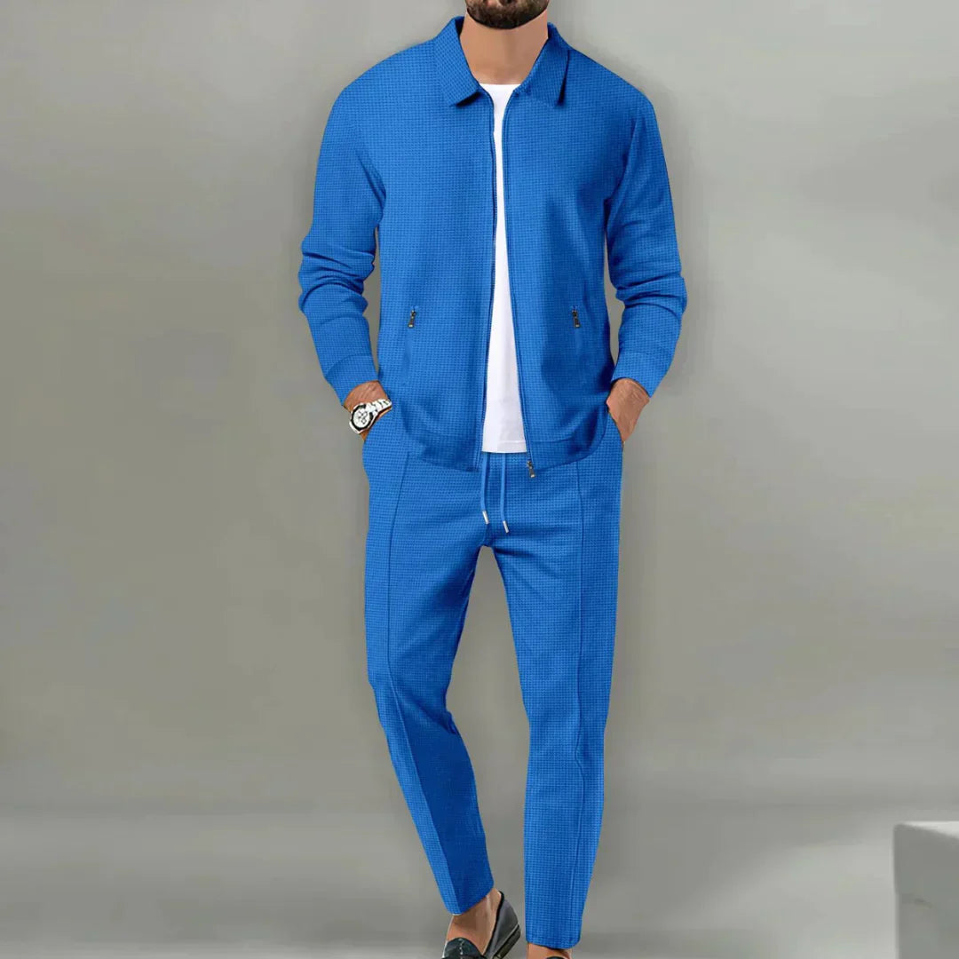 Mann in blauem Anzug mit Reißverschlussjacke und Hose, weißes T-Shirt, lässiger Stil.