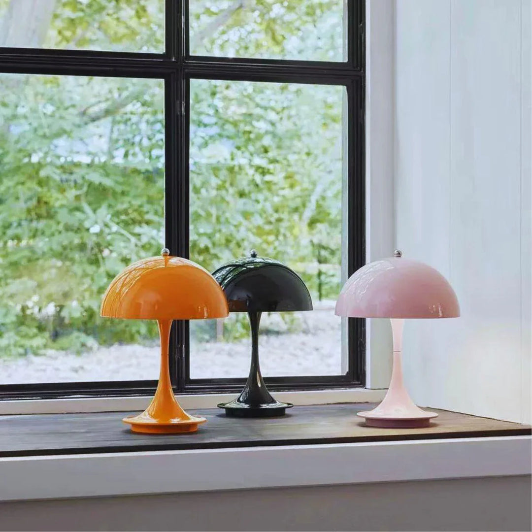 Drei bunte Tischlampen im Retro-Stil vor einem Fenster, orange, schwarz, rosa.
