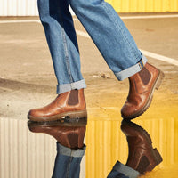 Braune Chelsea-Boots aus Leder, reflektiert in Pfütze, getragen mit blauer Jeans.