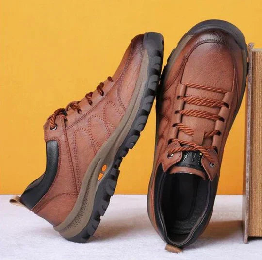 Braune Wanderschuhe aus Leder mit rutschfester Sohle vor gelbem Hintergrund.