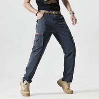 Mann trägt graue Cargohose mit Taschen, beige Stiefel, schwarzes T-Shirt, lässiger Stil.