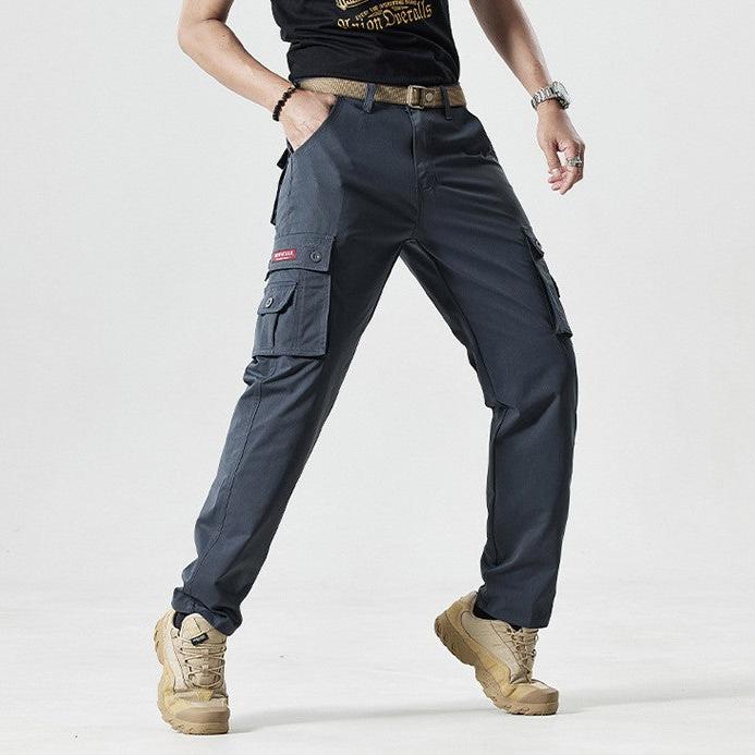 Mann trägt graue Cargohose mit Taschen, beige Stiefel, schwarzes T-Shirt, lässiger Stil.