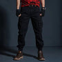 Mann in schwarzer Cargohose, rotem T-Shirt und braunen Stiefeln vor dunklem Hintergrund.