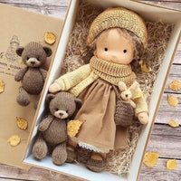 Handgemachte Waldorf-Puppe in brauner Kleidung mit Strickmütze und Teddybären in Geschenkbox.