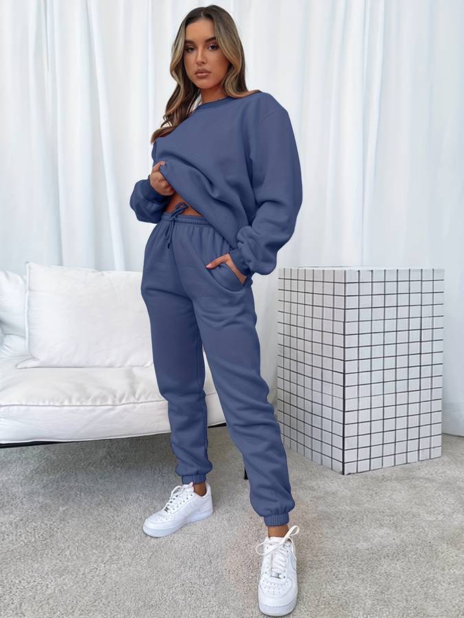 Frau in blauem Jogginganzug, weiße Sneaker, modernes Wohnzimmer, gemütliche Mode, Freizeitkleidung.