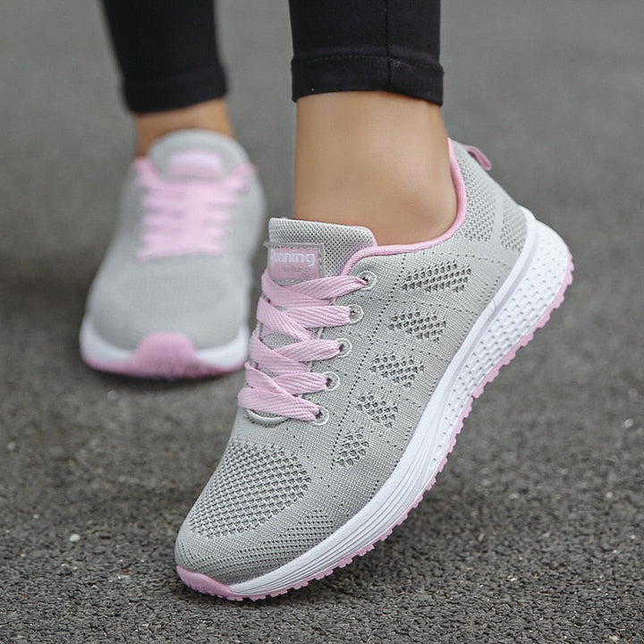 Graue Damen-Laufschuhe mit rosa Schnürsenkeln, atmungsaktiv, auf Asphalt.