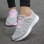 Graue Damen-Laufschuhe mit rosa Schnürsenkeln, atmungsaktiv, auf Asphalt.