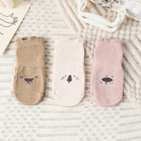 Drei Paar Baby-Socken, beige, creme und rosa, mit Tiermotiven, Baumwolle, auf Teppich.