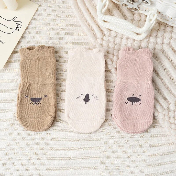 Drei Paar Baby-Socken, beige, creme und rosa, mit Tiermotiven, Baumwolle, auf Teppich.